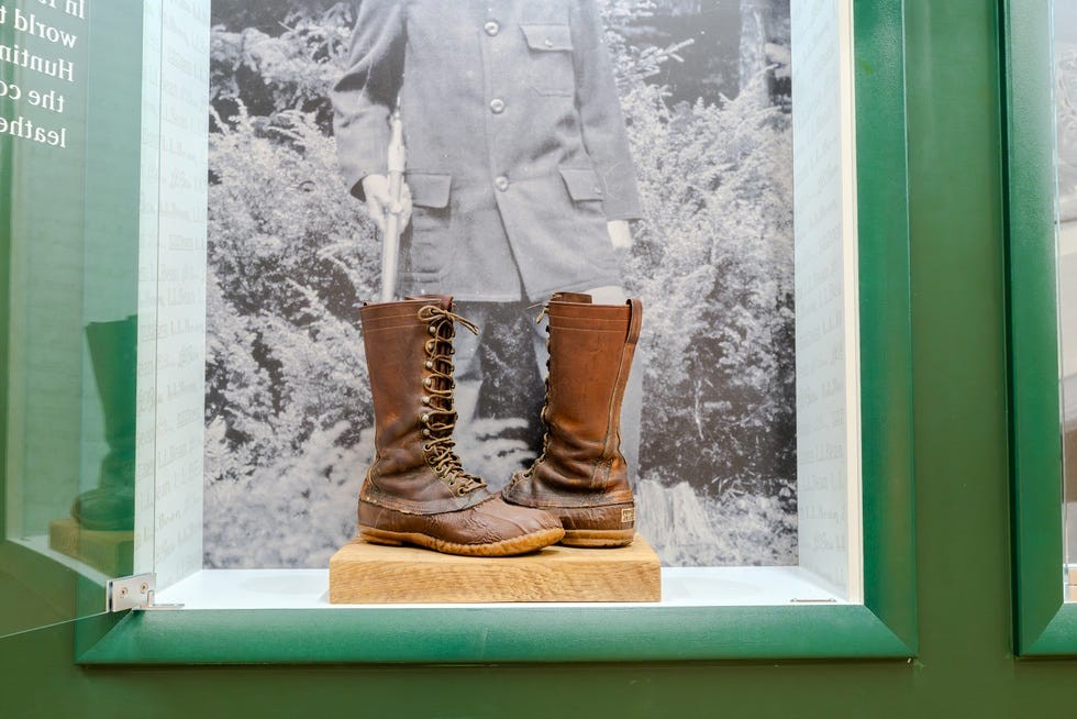 Historic brown leather boots displayed in a glass case with a black-and-white photo background.