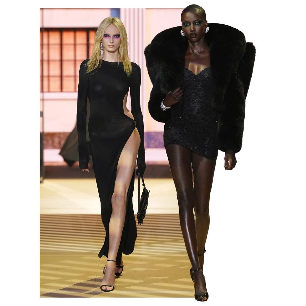 Two models walking on a runway wearing stylish outfits with dramatic lighting and a striking backdrop.