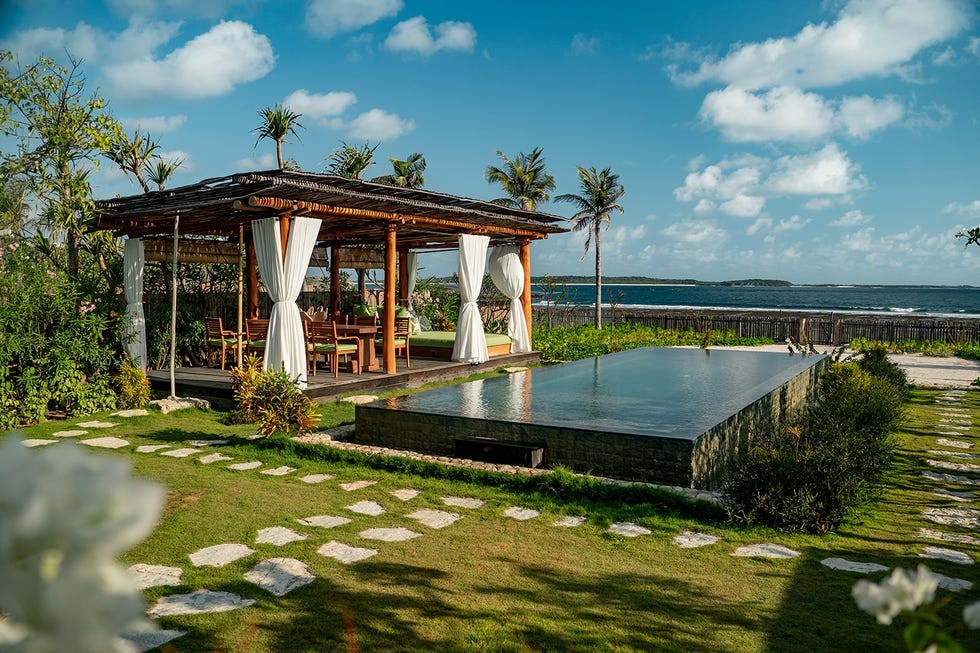 Nihi Rote Indonesia sister property of Nihi Sumba Modern outdoor relaxation area with a pool, wooden structure, and lush greenery near the ocean under a blue sky.