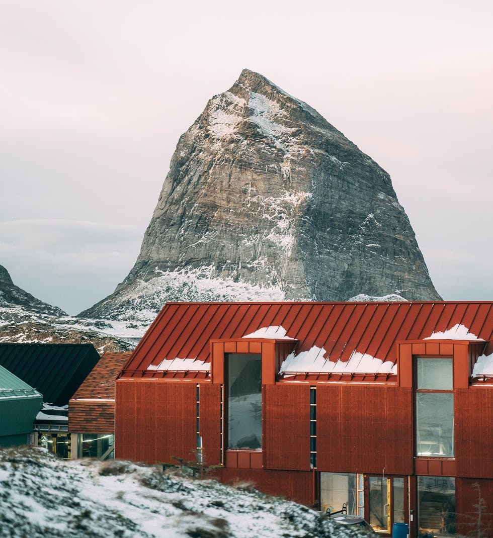 Ytri island Norway A snow-capped mountain rises above modern red buildings in a serene landscape.