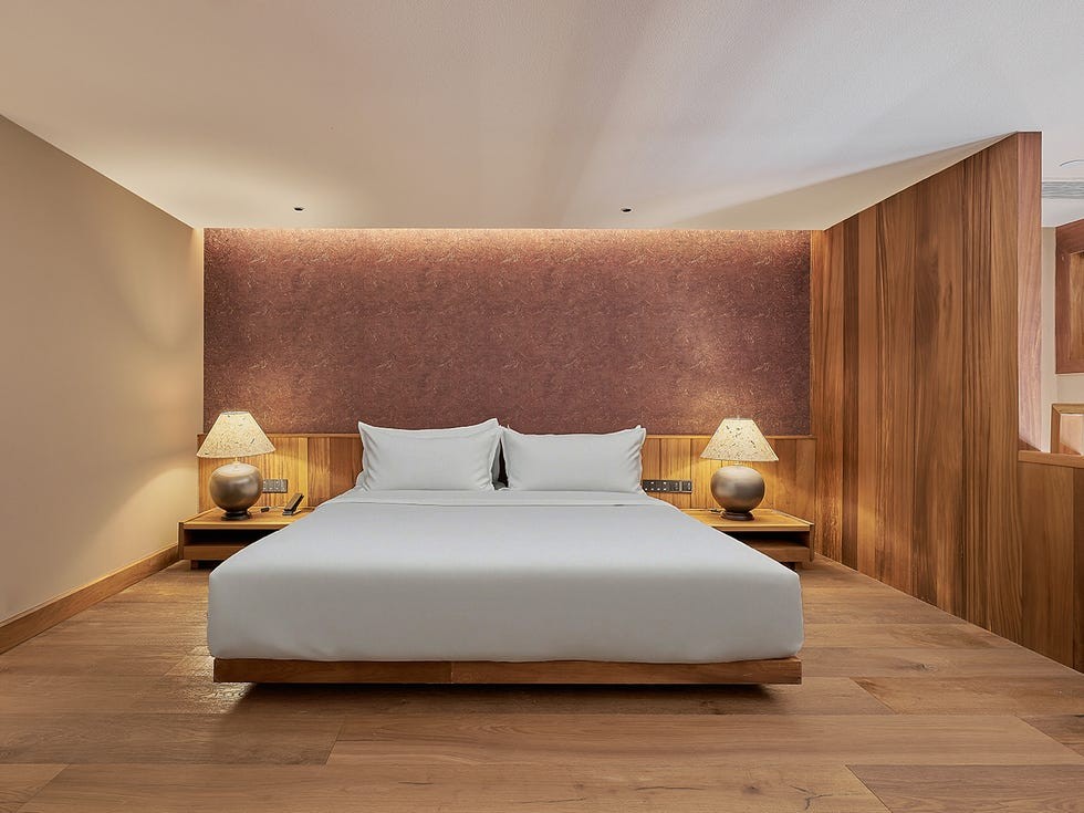 A Songtsam hotel interior, Kunming, China Modern hotel room featuring a queen-sized bed, wooden decor, and bedside lamps against a textured wall.