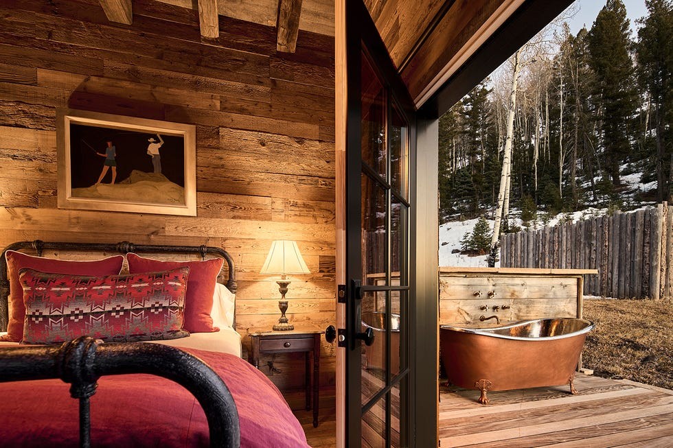 Trinchera Reserve & Lodge in Colorado Cozy bedroom featuring rustic decor, a copper bathtub outdoors, and scenic nature views through the open doorway.