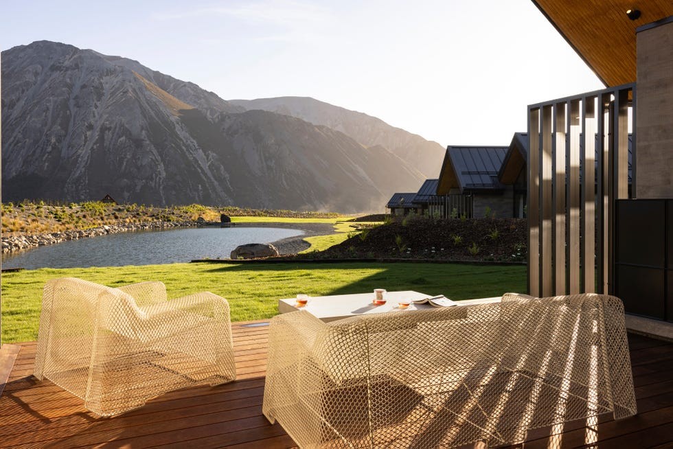 Flockhill Lodge New Zealand A serene outdoor seating area overlooking a picturesque lake and mountains during sunset.
