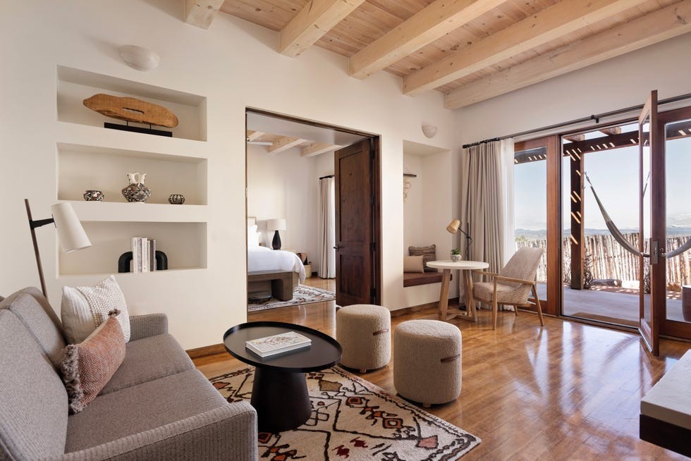 Brightly lit, modern living space featuring a sofa, coffee table, decor shelves, and a view of the outdoor patio with a hammock.