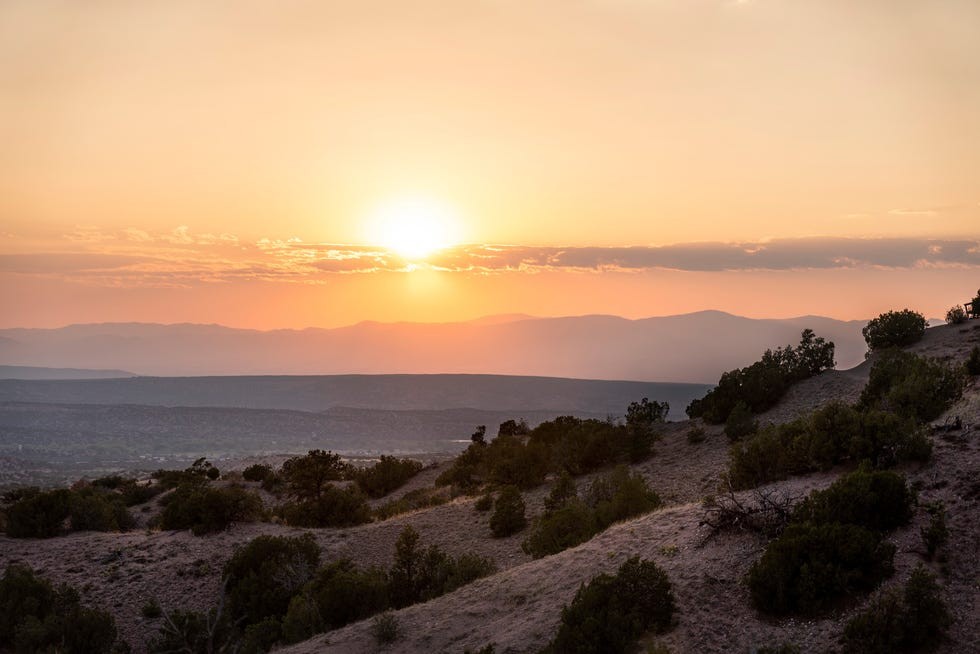 Sunset over rolling hills and distant mountains, with warm orange and pink hues filling the sky.