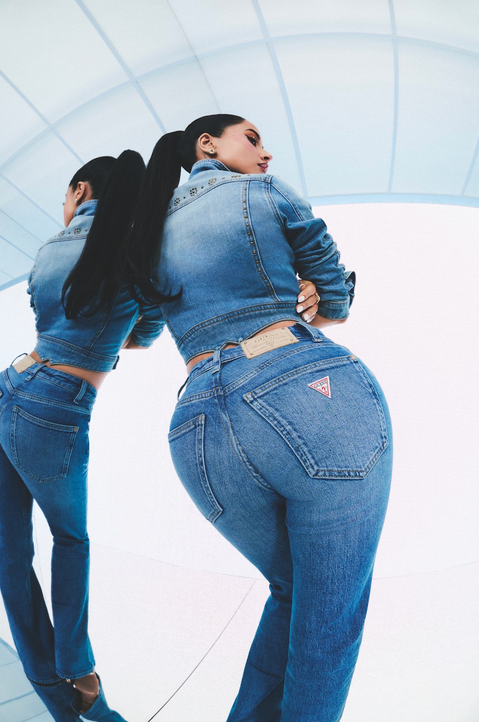 Woman in a denim jacket and jeans, posing with a reflective background.