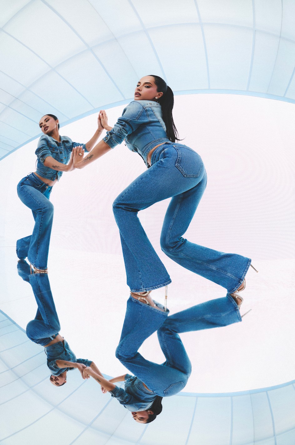 Model in a denim outfit poses against a reflective surface with an abstract background.