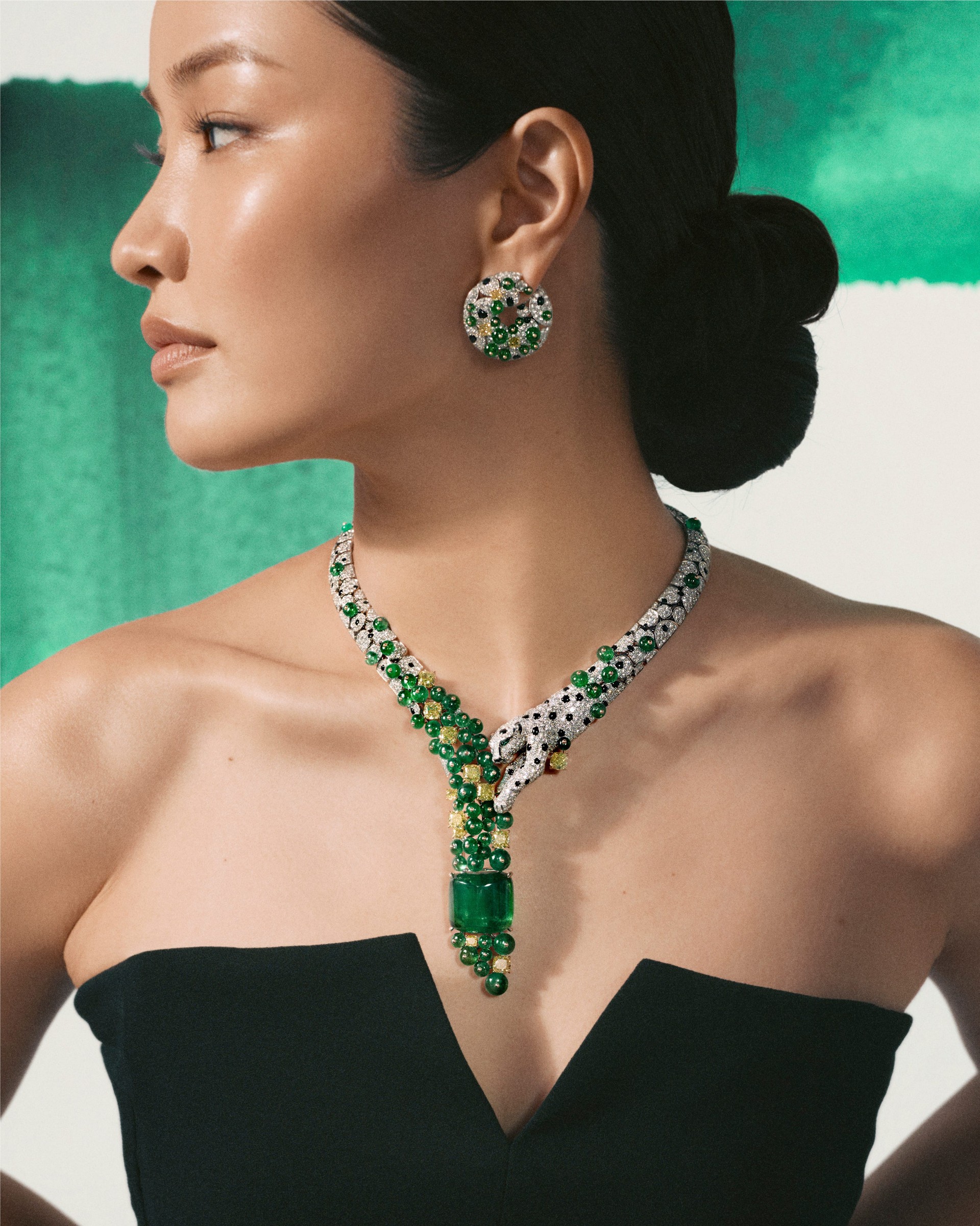 Elegant woman showcasing a statement necklace and earrings with green gemstones against a stylish background.