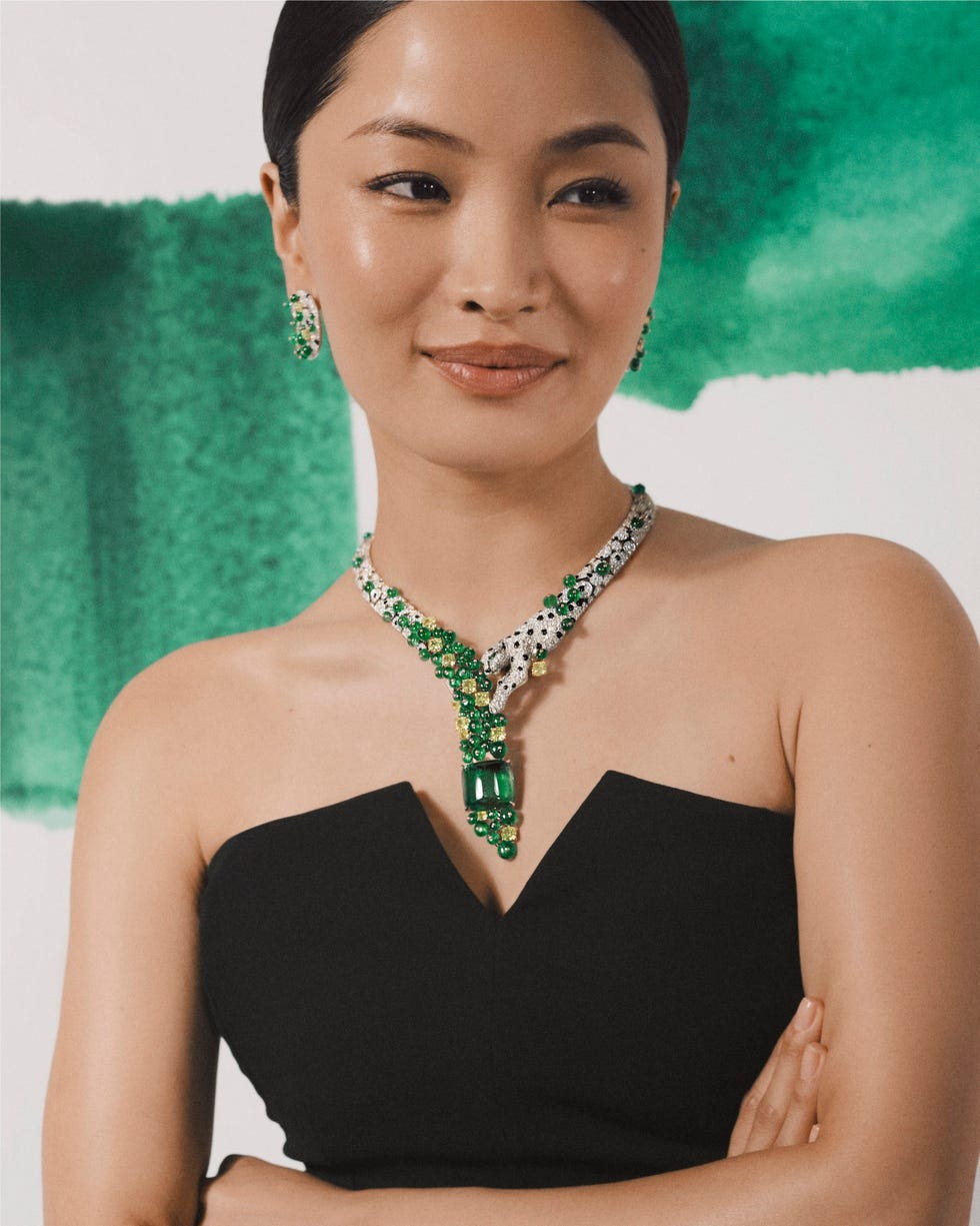 Model wearing elegant jewelry with green stones and a black strapless dress, set against a colorful background.