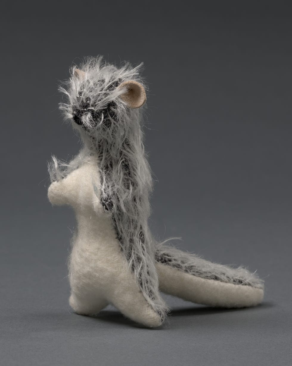 Handcrafted plush figurine resembling an animal with gray and white fur, standing upright against a dark background.