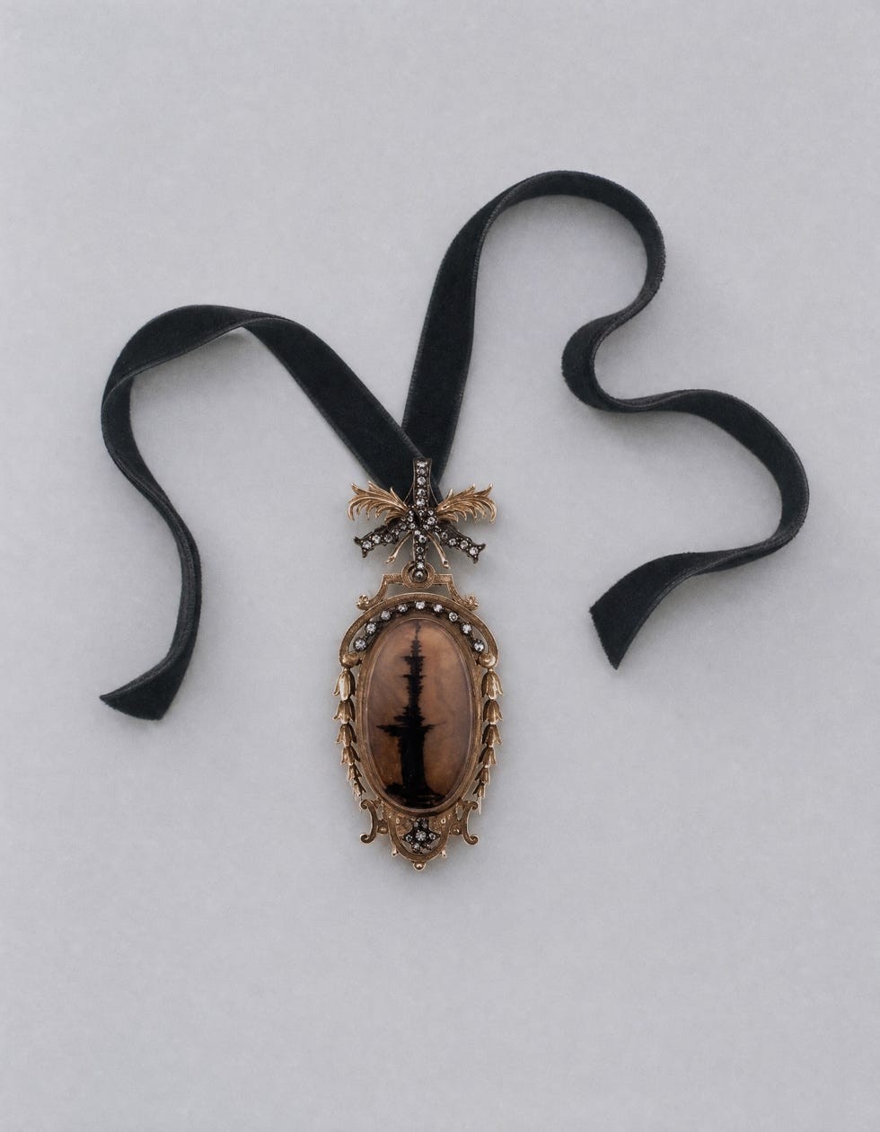 A decorative pendant with an oval stone and intricate metalwork, suspended from a black ribbon.