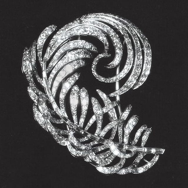 Detailed silver brooch with a swirling leaf design, encrusted with sparkling gemstones on a black background.