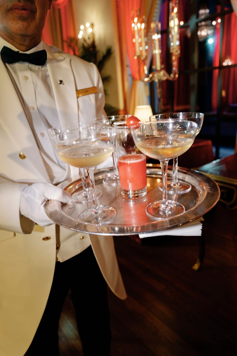 A tray held by a waiter with multiple cocktails and a fruit garnish in an elegant setting.