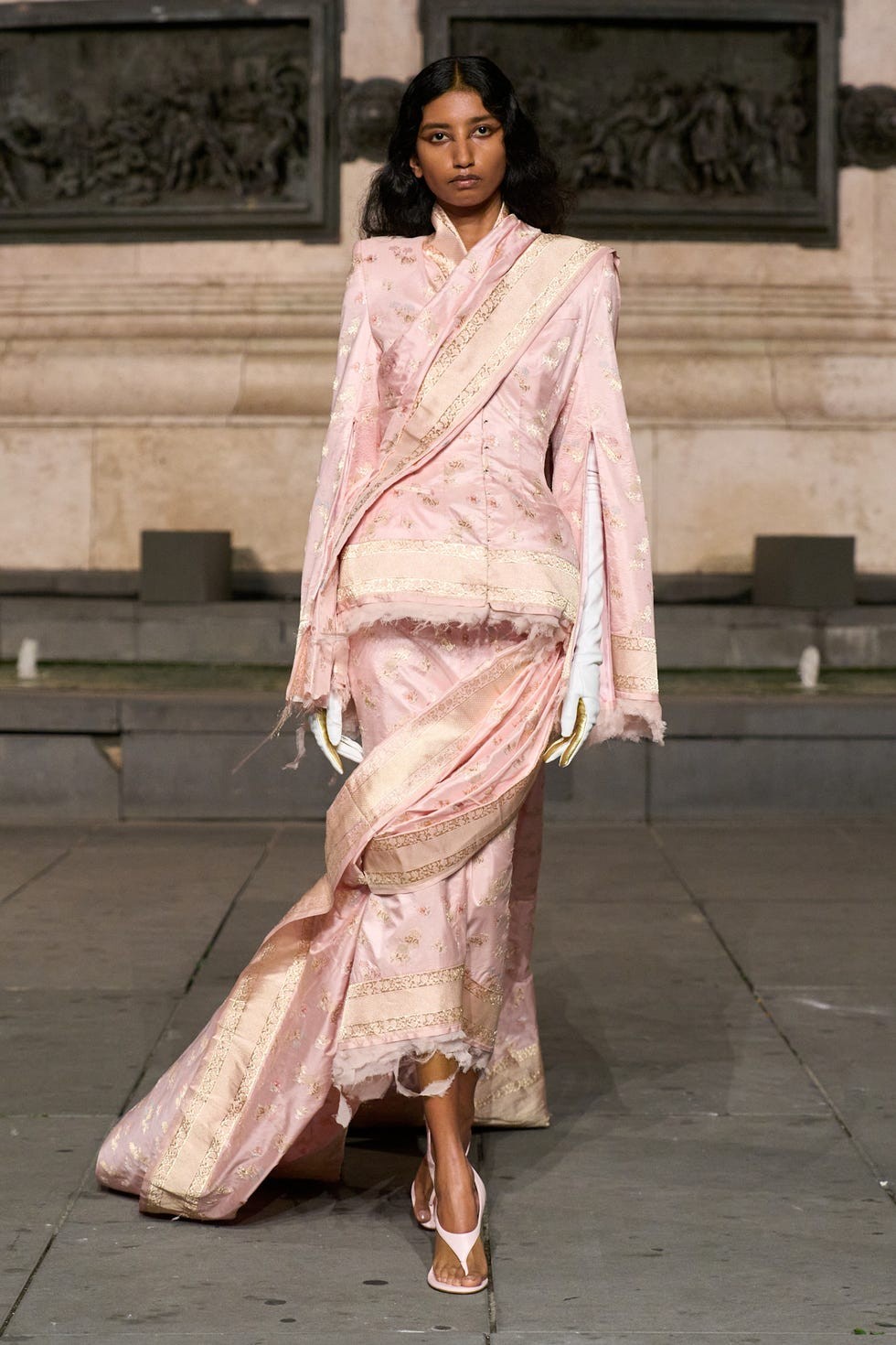 Model showcasing an elegant pink outfit with intricate detailing on a runway.