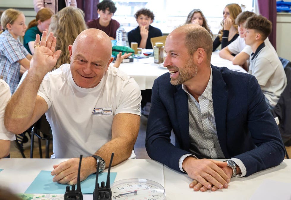 Two men smiling and engaging in conversation at a table with young people in a classroom setting.