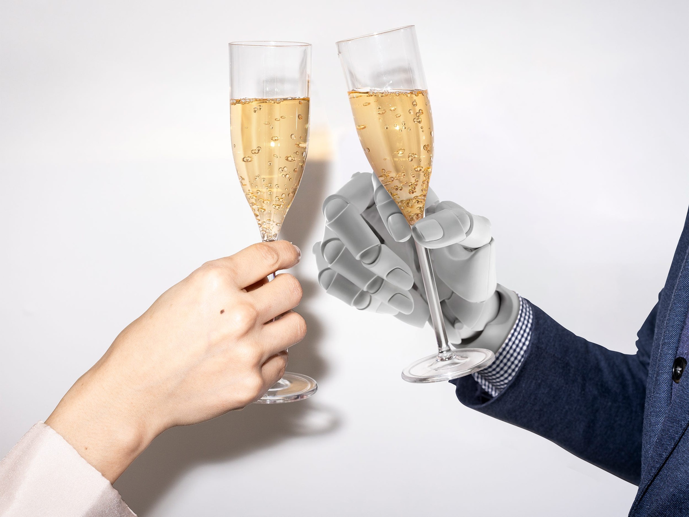 Cheers with champagne flutes, one held by a human hand and the other by a robotic hand.