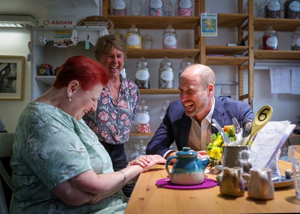 Three people sharing a joyful moment in a café, with a teapot and flowers on the table.