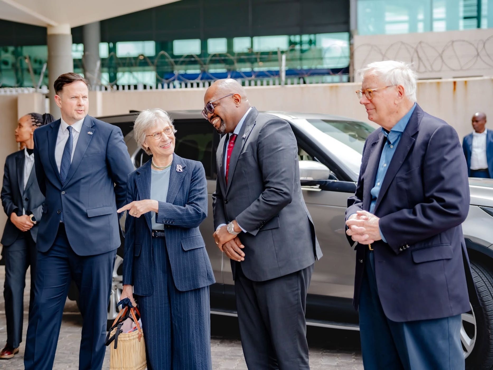 A group of professionals engaged in a lighthearted conversation outside a vehicle in an urban setting.
