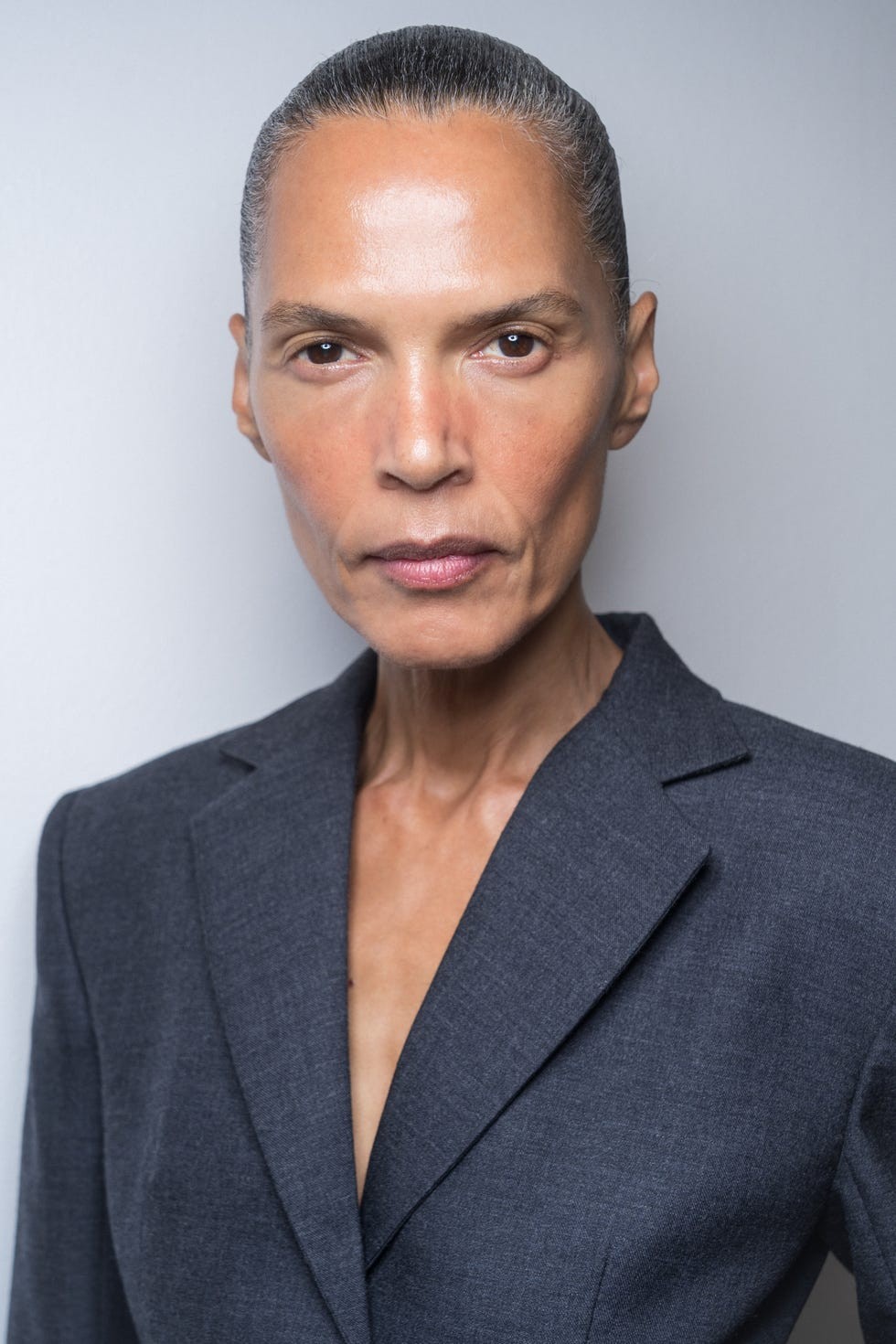 Person in a gray blazer with a neutral expression facing forward.