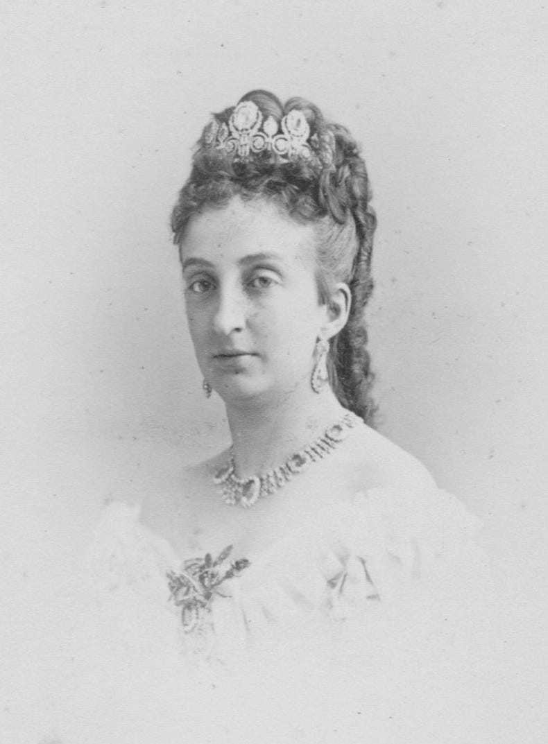 Young woman in an elegant gown with elaborate jewelry and a decorative hairpiece, posed against a light background.