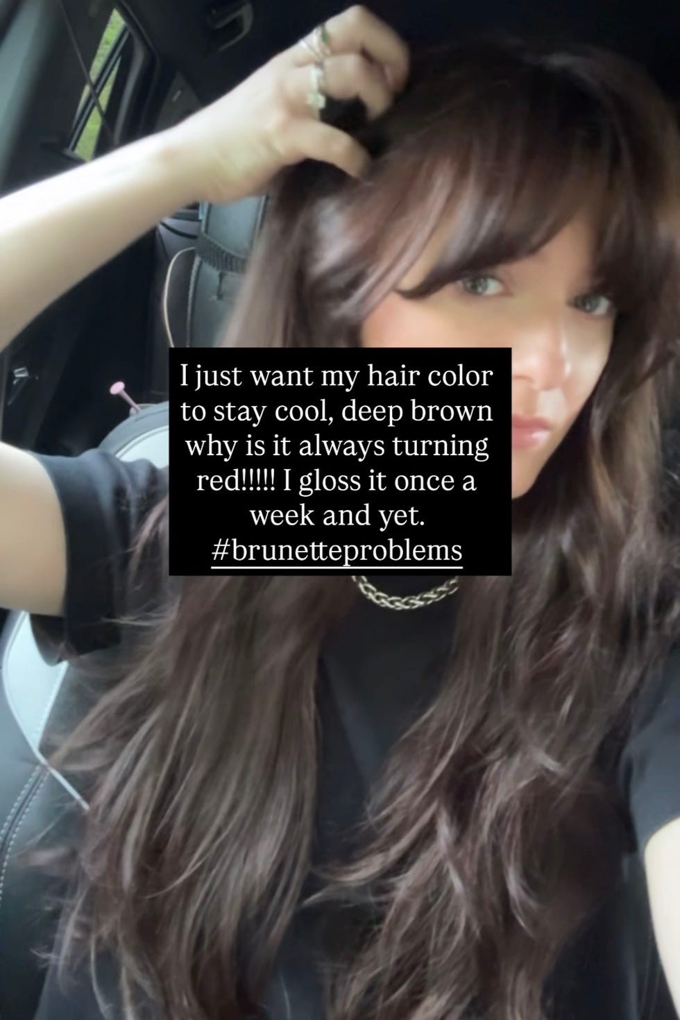 Woman with long brown hair expressing frustration about hair color changing, wearing a black shirt in a car.