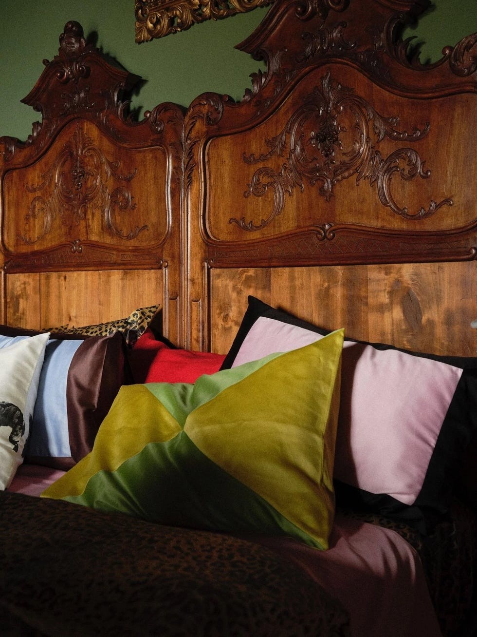 Ornate wooden bed frame with colorful pillows in various fabrics and patterns.