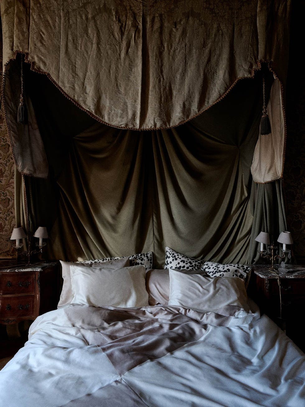 Luxurious bedroom with a draped headboard, soft bedding, and decorative pillows in a rich, muted color palette.
