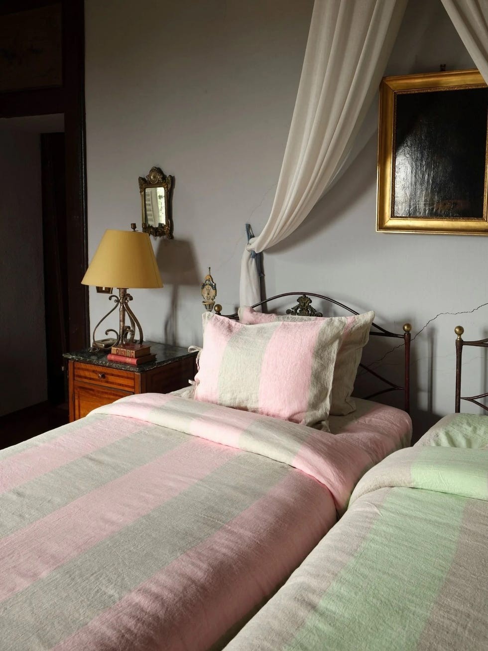 Two beds with pastel-colored striped bedding and a vintage lamp in a softly lit room.