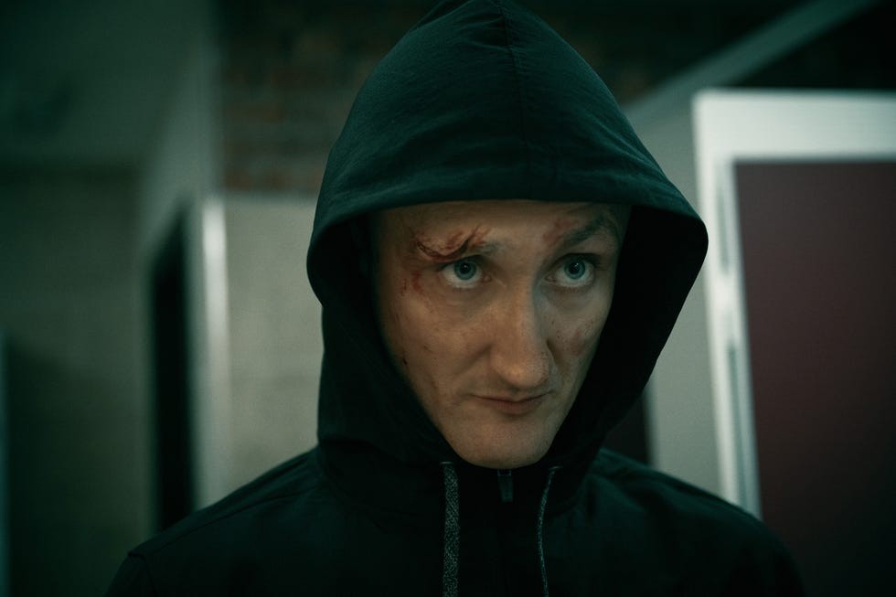 A person with a hoodie and visible facial injuries looking intently at the camera.