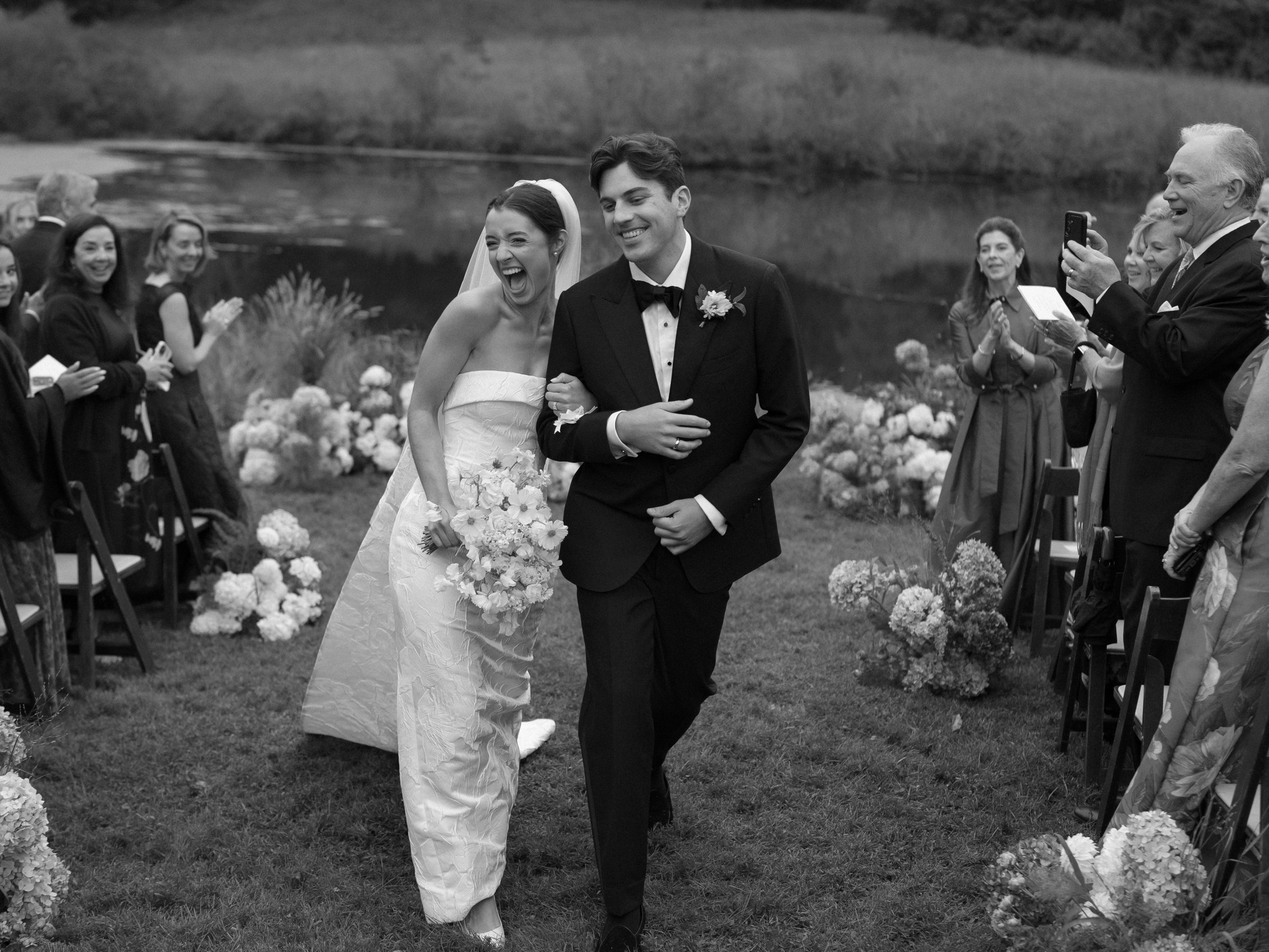 A joyful bride and groom walking together after their wedding ceremony, surrounded by guests and floral decorations.