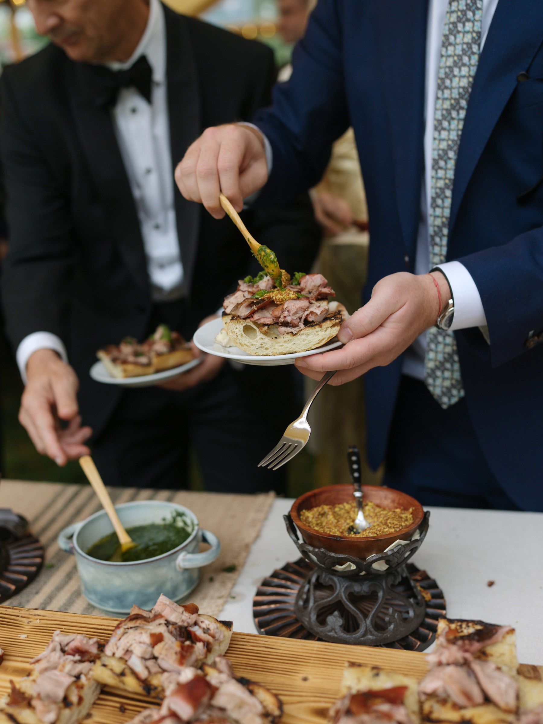 A person garnishing a plate of meat on bread with sauce at a gourmet outdoor event.