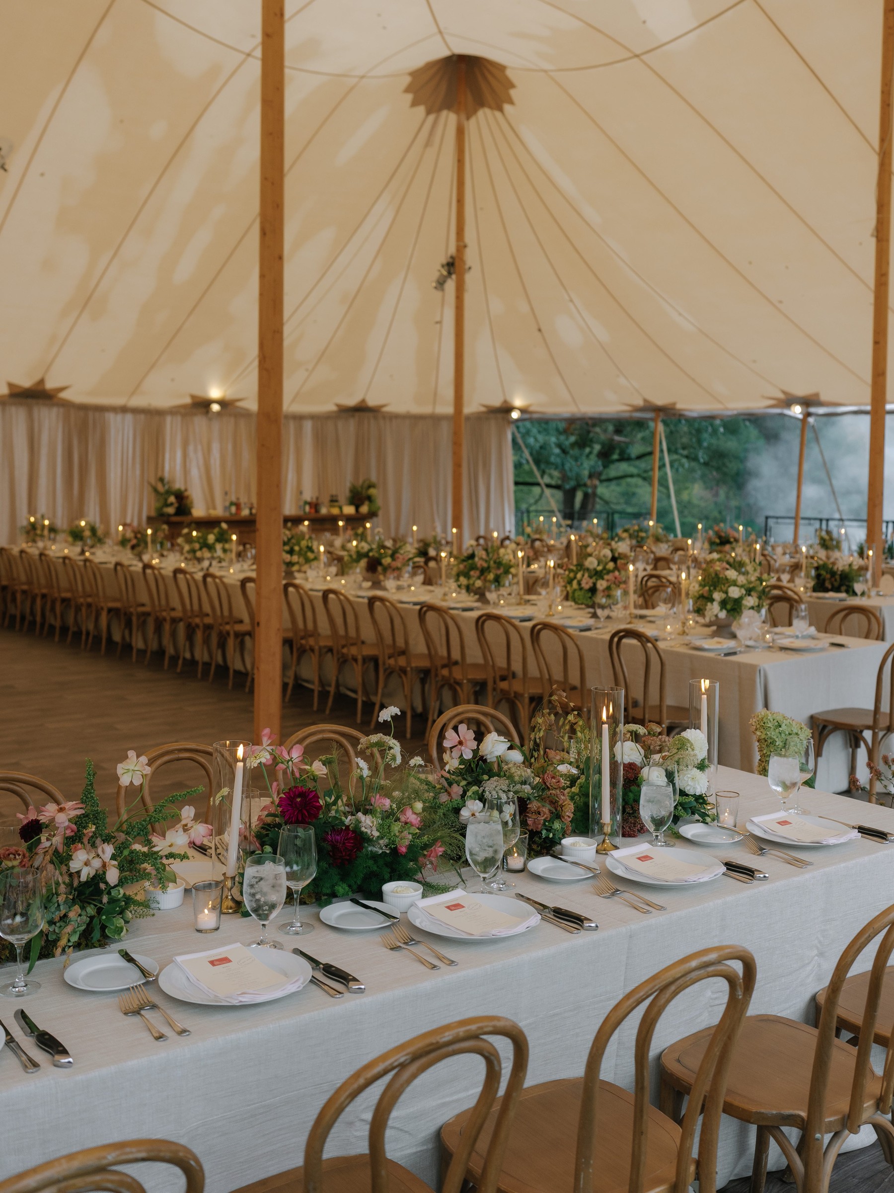 Elegant dining setup with floral arrangements and candles under a large tent.