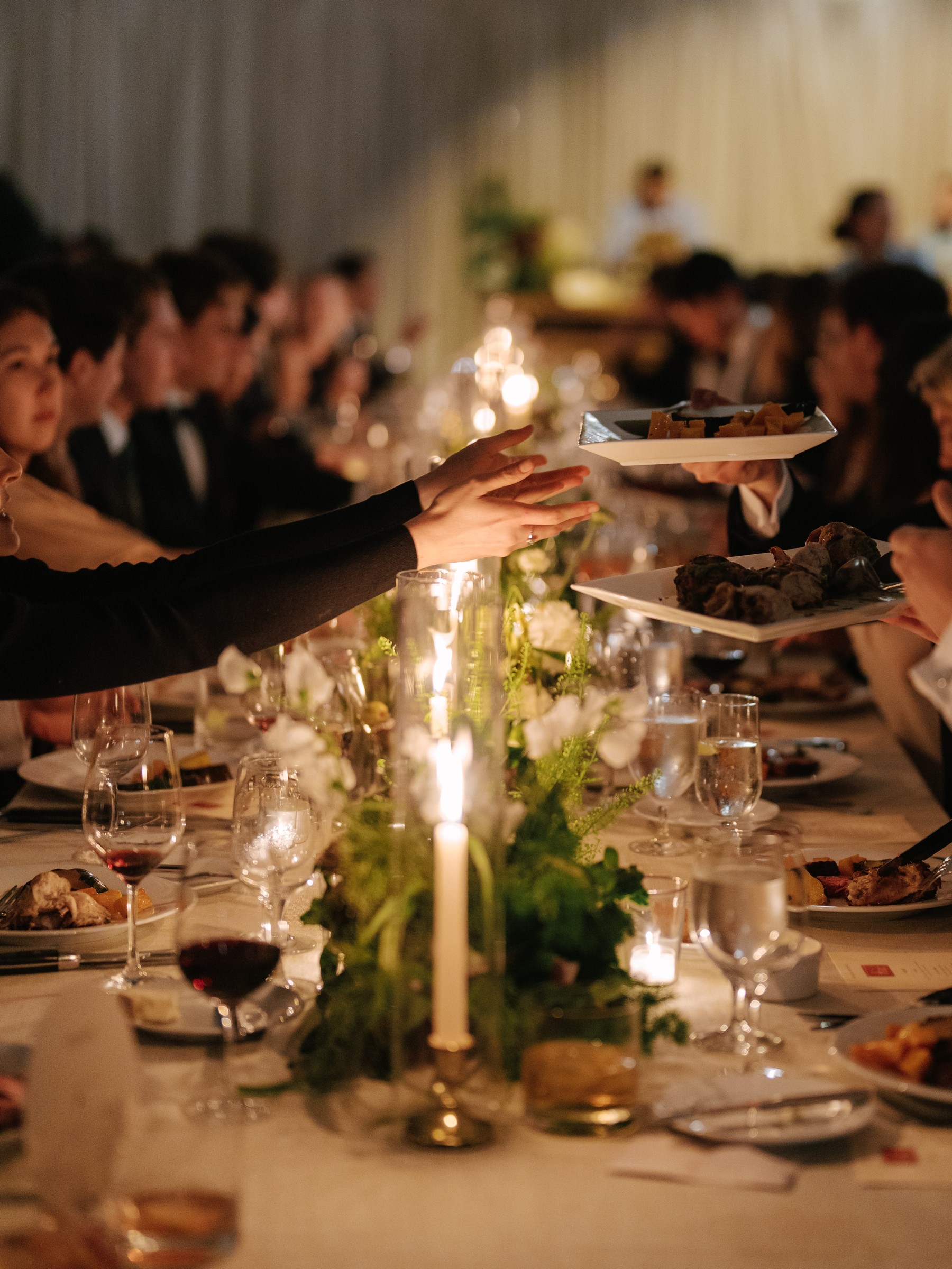 A elegantly set dining table with guests enjoying a meal, candlelight, and floral decorations.