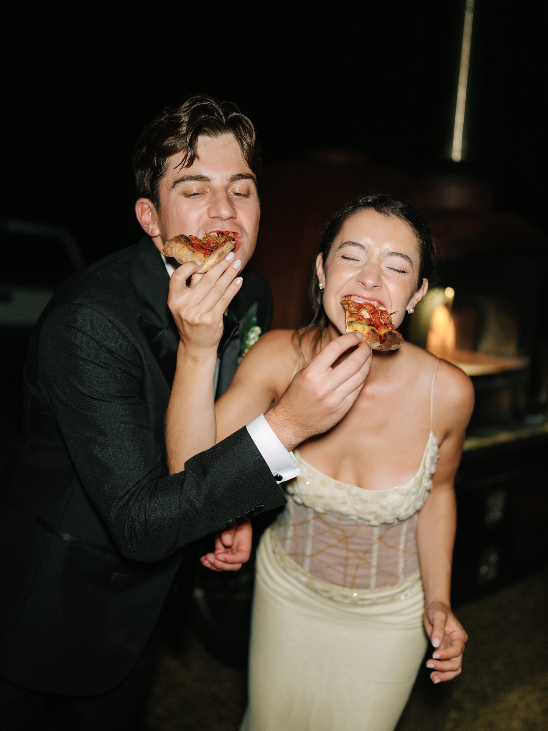 Couple enjoying pizza at night, smiling and sharing a fun moment together.