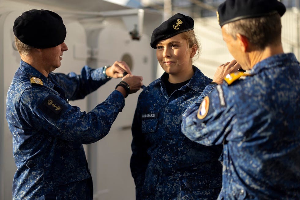 Military personnel awarding a service insignia to a young woman in uniform on a naval vessel.