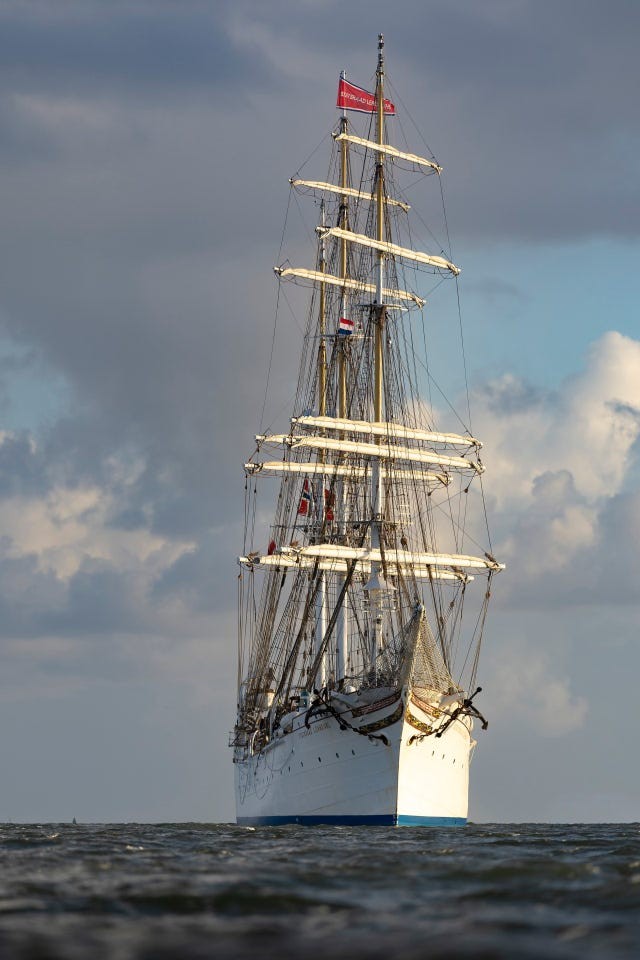 Tall ship sailing under cloudy skies, with prominent sails and flags displayed.