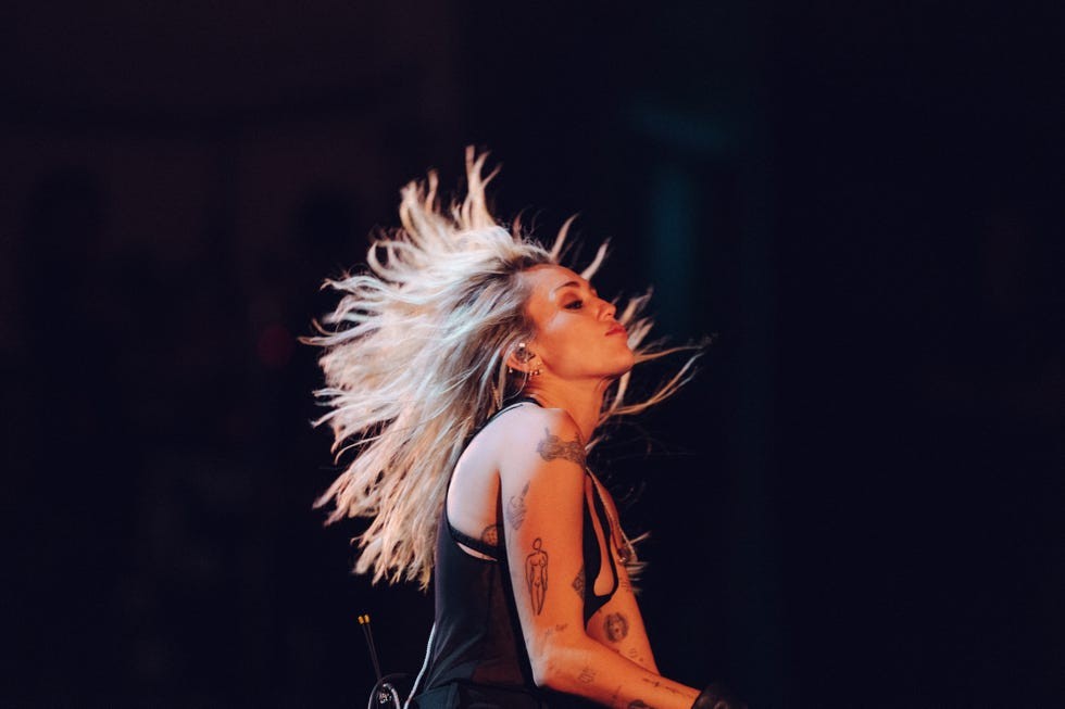A musician performing energetically with flowing hair and visible tattoos on stage.