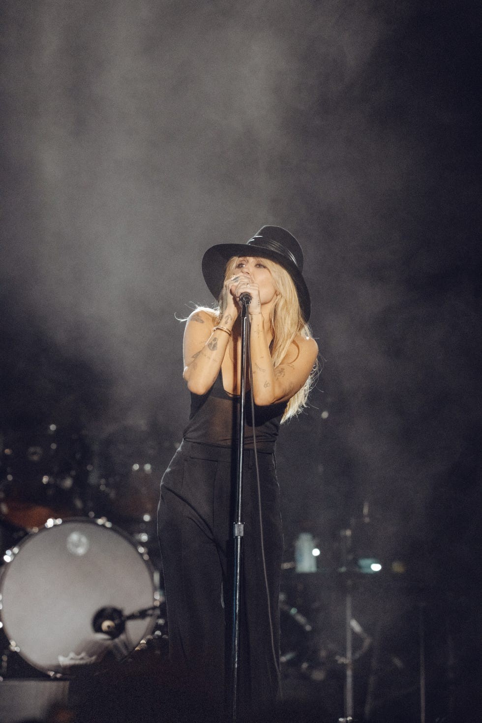 A singer performing on stage in a hat, with dramatic lighting and smoke in the background.