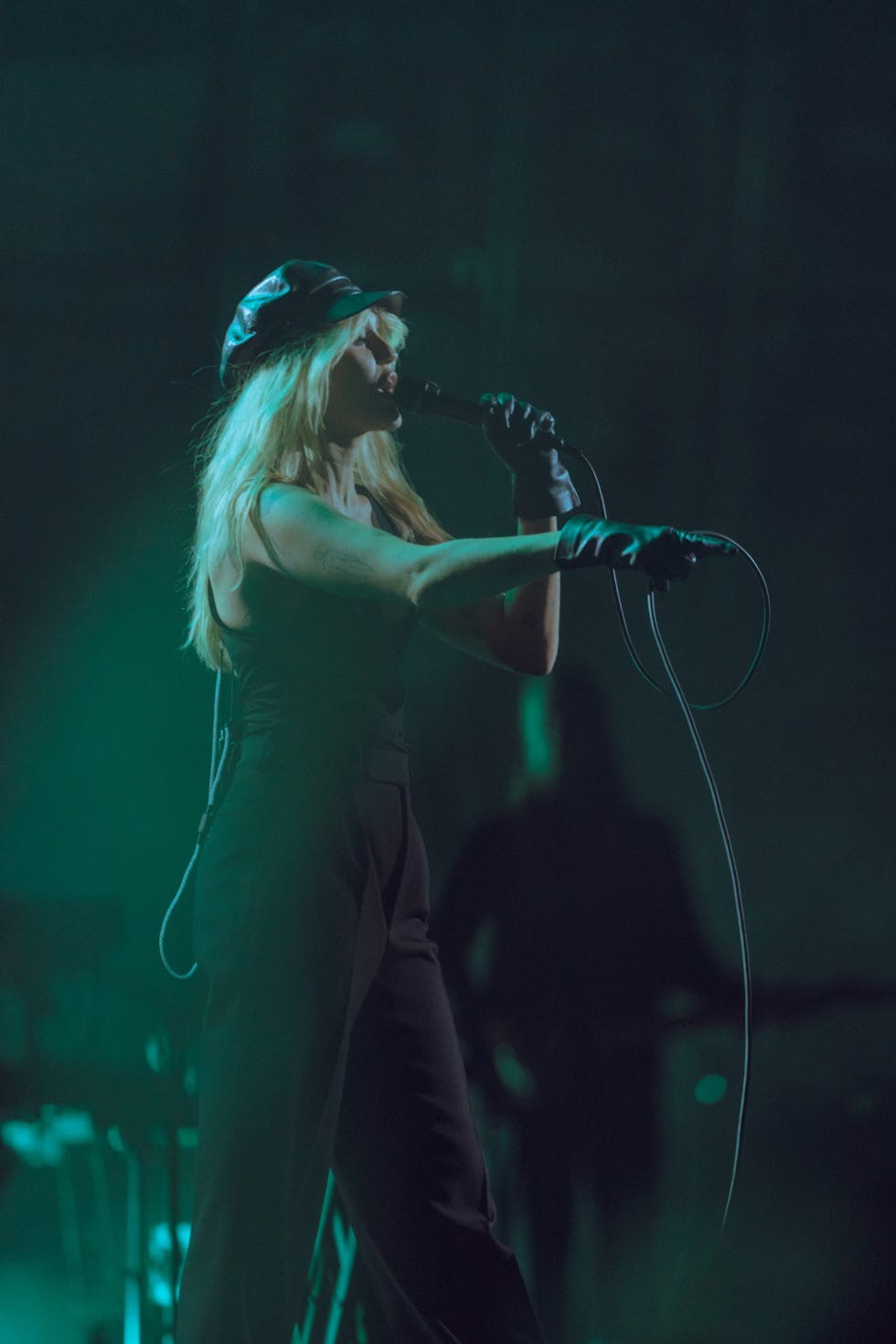 Singer performing on stage with a microphone, wearing a hat and gloves, surrounded by a moody, green atmosphere.