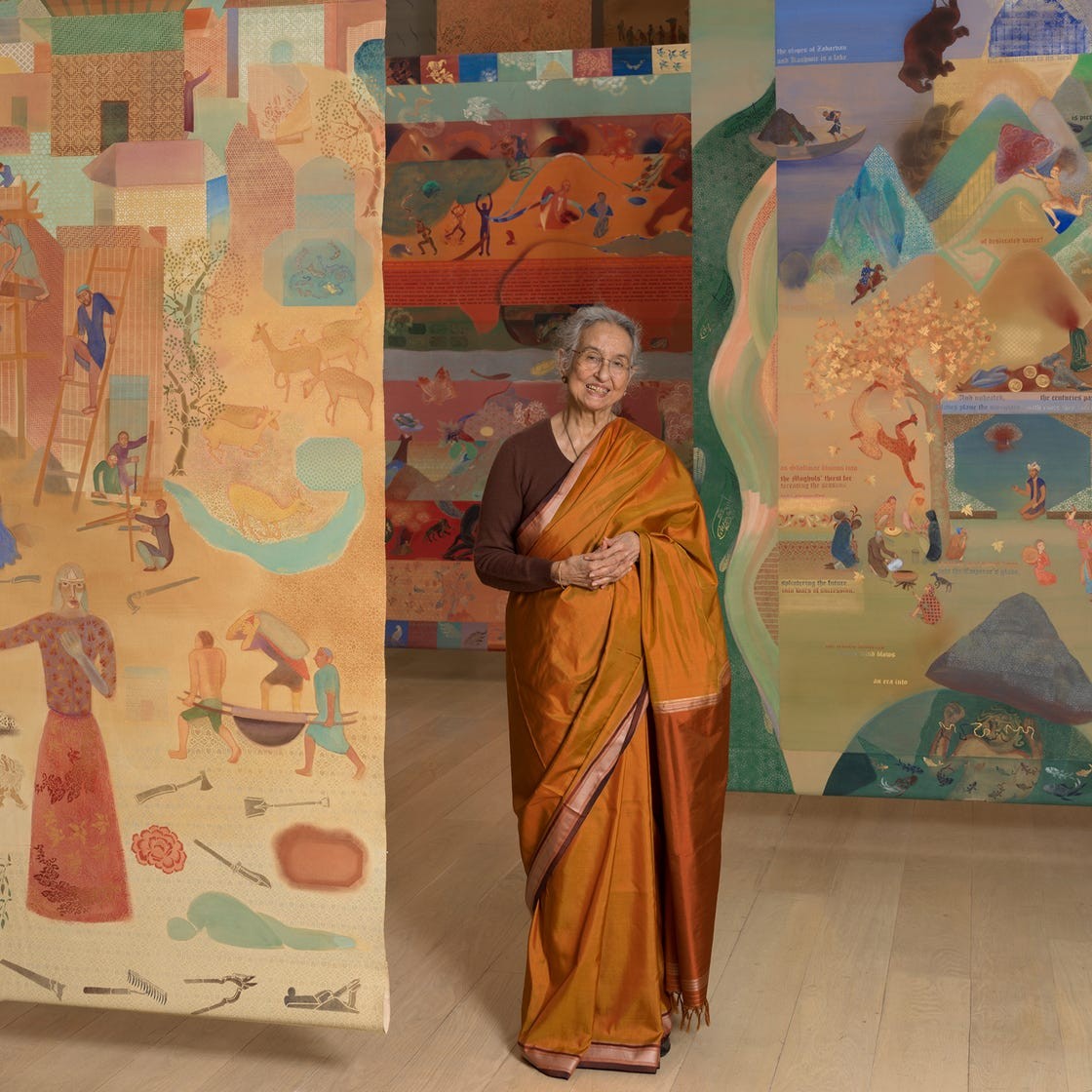 Elderly woman in traditional attire smiling, surrounded by colorful murals depicting cultural scenes.