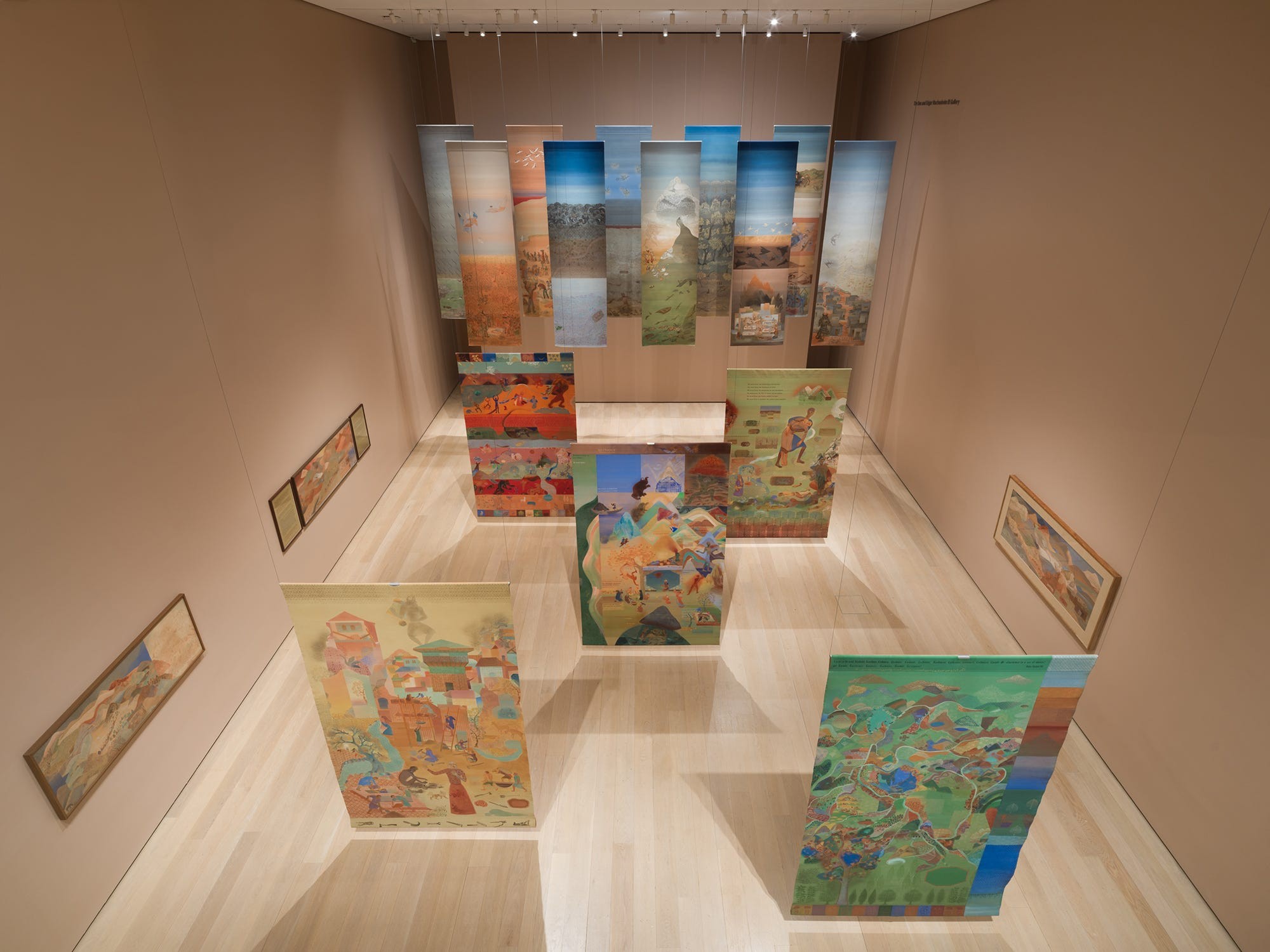 Exhibition space featuring hanging and standing colorful artworks on display in a light-filled gallery.