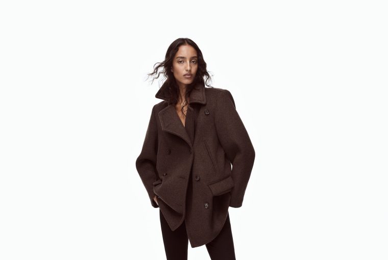 Model wearing a dark brown oversized coat with a high collar, posing confidently against a plain background.