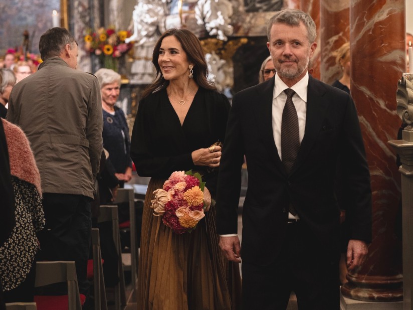 A stylish couple walking in a decorative venue, with one holding a bouquet of flowers.