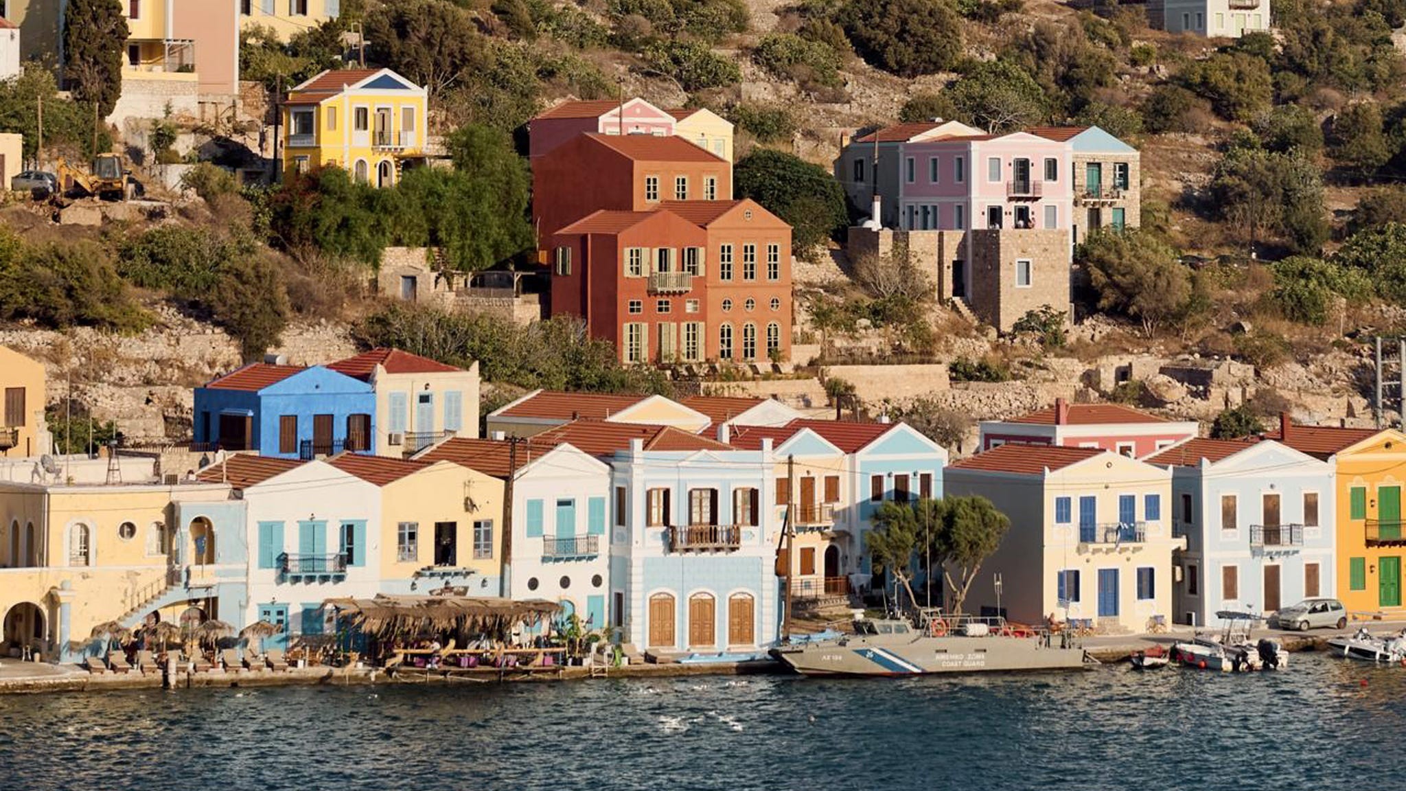 Colorful houses lining the waterfront on a Mediterranean hillside under a clear sky.
