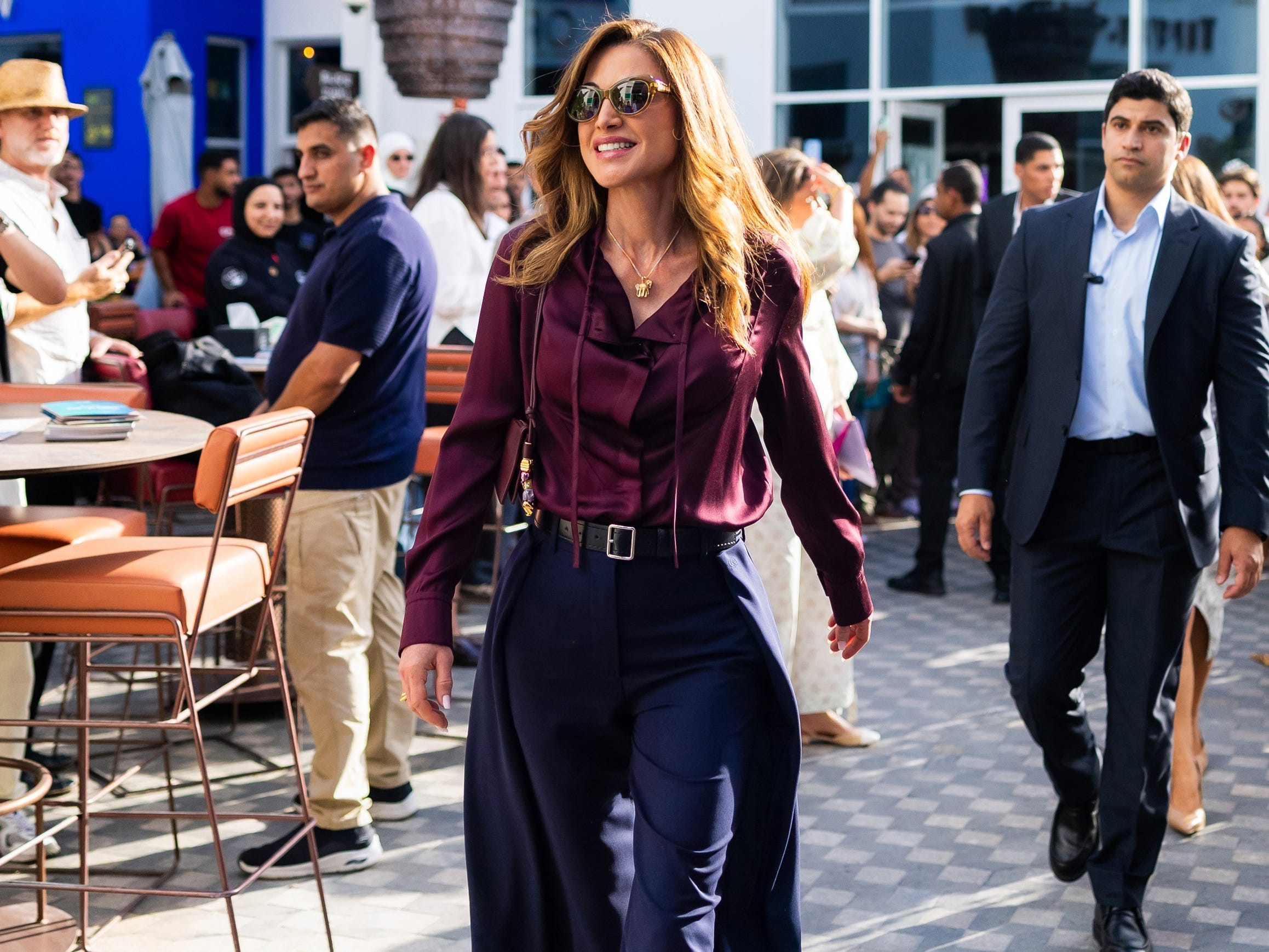 Person walking confidently in a stylish outfit, surrounded by a crowd in a vibrant outdoor setting.