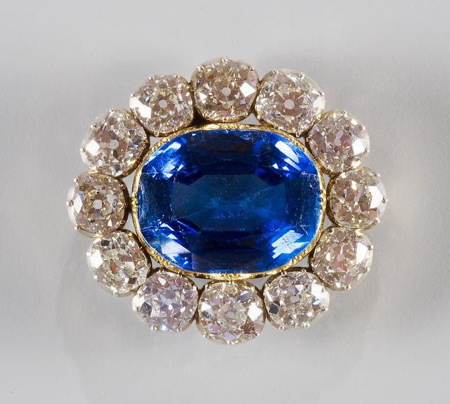 A large blue gemstone surrounded by smaller sparkling diamonds in a decorative setting.