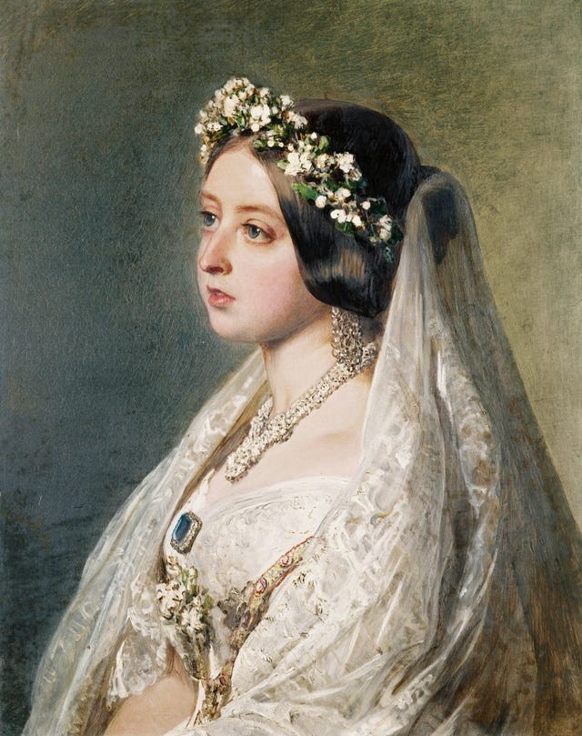 A young woman in a bridal gown adorned with a crown of flowers and jewelry, gazing to the side.