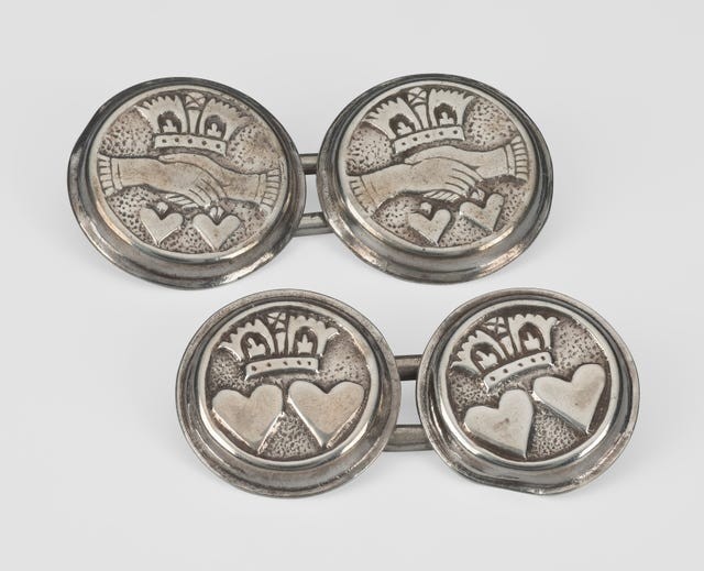 Four decorative silver buttons featuring intertwined hands and hearts, adorned with crowns and intricate designs.