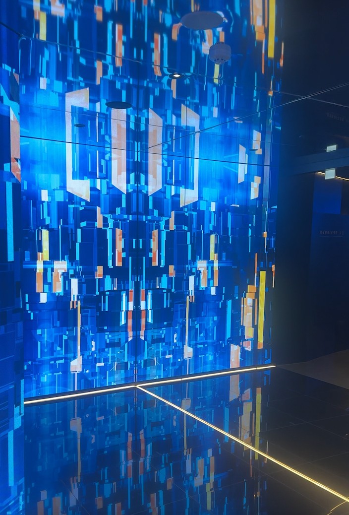 Vibrant blue digital wall with geometric patterns and reflections on a dark floor.