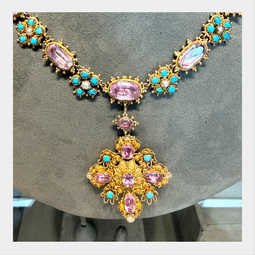 Intricate gold necklace featuring pink and turquoise stones, with a decorative pendant in the center.